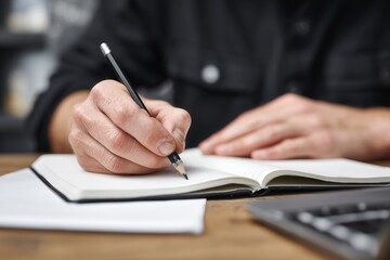 a person writing in an open notebook on the table, with their hands holding a pencil and computer beside them Generative AI