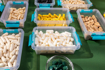 Vitamins, minerals and dietary supplements in containers from above on green background in sunlight. Assortments of many colored pills, tablets, capsules and food supplements.