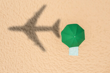 Green umbrella and striped towel on beach, top view. Flying airplane casting shadow on sand