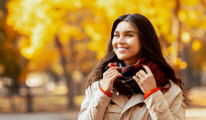 Beautiful millennial lady in coat and warm scarf enjoying colorful change of seasons in autumn park. Smiling young woman walking outside on beautiful sunny fall day