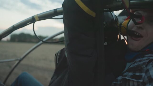closeup of excited man in helmet and goggles gripping paramotor cage with open mouth as engine revs against blurred sky and field background moments before flight takeoff