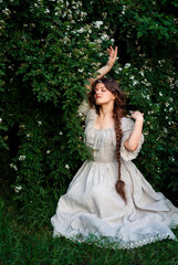 Fototapeta premium Beautiful woman with long braid in vintage dress posing in jasmine flowers in countryside 