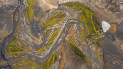 Aerial view of braided river channels flowing through volcanic valley in Iceland with rocky terrain and patches of green moss landscape