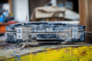 old, weathered suitcase, marked by time and dust, sits on a vibrant, weathered surface, suggesting...