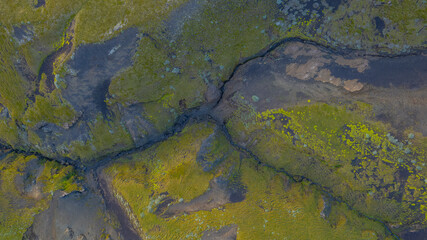 Top down aerial of green moss wetlands in Iceland with dark volcanic soil and small rivers creating abstract natural textures in landscape