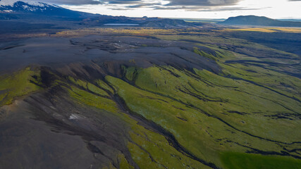 Fototapeta premium Aerial shot of Icelandic wilderness with volcanic slopes layered in black ash and green moss creating striking natural patterns