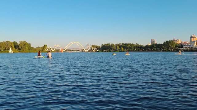 KYIV, UKRAINE, AUGUST 31, 2025: People floating on SUP boards on the Dnieper River in Kyiv city, near Wave Bridge and Obolonsky Island. Stand Up Paddleboard. Video footage from floating yacht