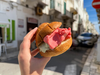 Famous Sicilian Brioche bun with pistachio and strawberry Ice Cream Gelato in the female hand close up on the street of Polignano a Mare, Italy