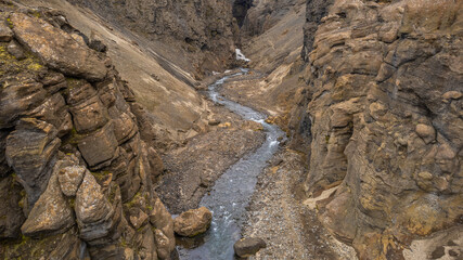 Dramatic volcanic canyon in Iceland with a narrow river flowing between steep rugged cliffs and barren rock formations in the highlands