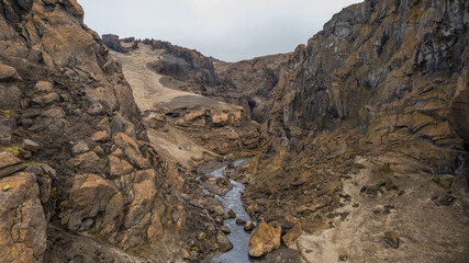 Scenic volcanic canyon landscape in Iceland with river carving through rocky terrain showing erosion patterns and rugged highland geology