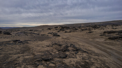 Icelandic highland desert with rock formations and distant mountain range under dramatic cloudy sky in remote untouched nature