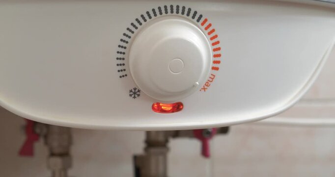 Regulator for heating cold water in boiler. Man turns temperature control on heater of water. Red light indicator comes off, boiler has turned off. Boiler heats water from cold water supply system