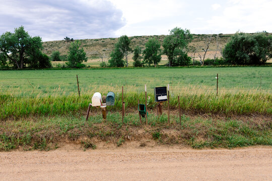 Multiple roadside mailboxes attached to wooden posts along a dirt road