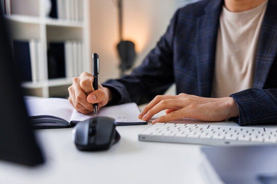 Man writing in notebook at desk with computer peripherals.