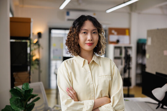 Confident woman with crossed arms in modern office setting.