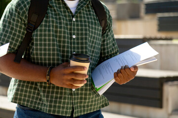 University student holding coffee and documents walking on campus