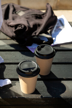 Two disposable coffee cups sitting on a wooden table in the sunlight