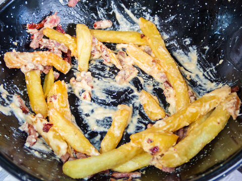French fries with cheese sauce and bacon lying in a black pan