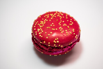 Colorful macarons on white floral plate against warm textured background. Red, beige, and chocolate tones with visible fillings. Cozy and inviting dessert still life.