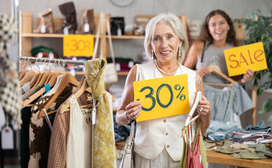 Portrait of mature woman holding sign saying 30 percent discount in clothing store