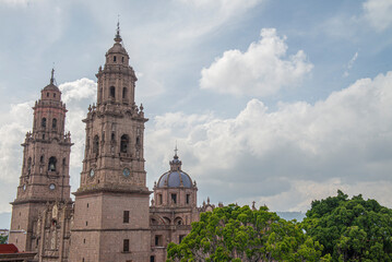 Obraz premium Streets, landscapes, and architecture of Morelia, Michoacan, Mexico, Pink quarry towers of the cathedral in the historic center with a blue sky with clouds. Horizontal or panoramic view
