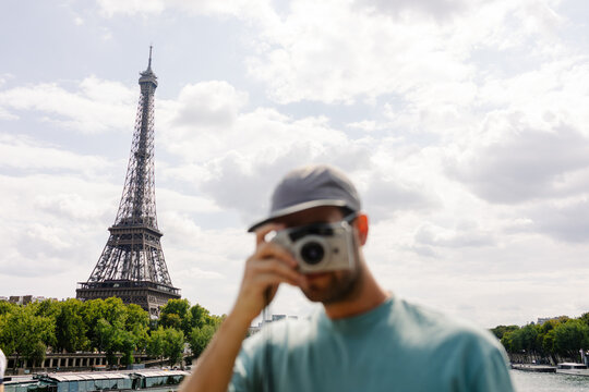 A tourist posing with an analog camera in front of the Eiffel Tower 