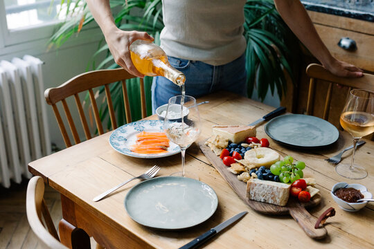 Woman pouring wine into glasses beside a plate with French cheeses