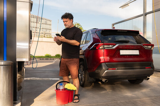 Man Using Phone at Self-Service Car Wash in the City