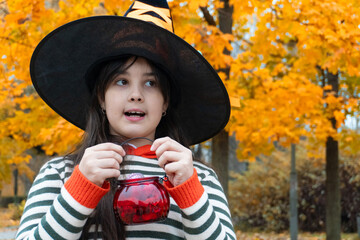 Young girl in witch hat celebrating halloween in autumn park