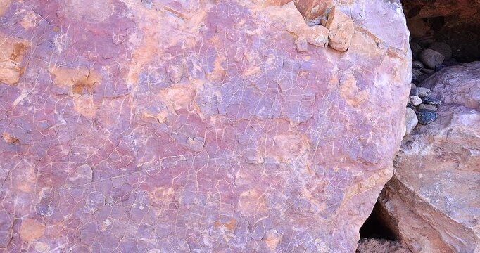 Closeup motion shot of rough surface of pink and rust color rock with extensive abstract crack pattern in dry stack wall 4k