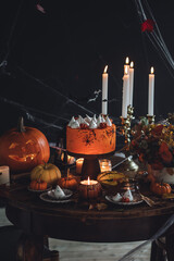 Homemade delicious chocolate cake with coloured orange cream and meringue ghosts, pumpkins for Halloween home party. Elegant beautiful table arrangement with candles, chandelier, Jack-o-Lantern