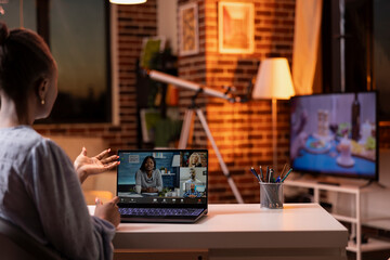 Self employed woman joins video conference with diverse professionals, working remotely in brick wall apartment. Female entrepreneur doing business presentation during virtual meeting with clients.