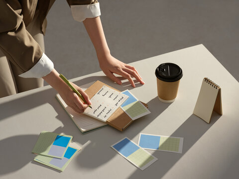 A person is writing on a notepad with sticky notes and a coffee cup