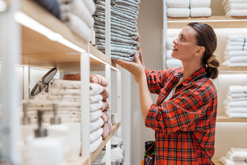 Woman in red plaid shirt organizing neatly stacked towels on shelves in a retail store, showcasing attention to detail and commitment to presentation in a home goods environment