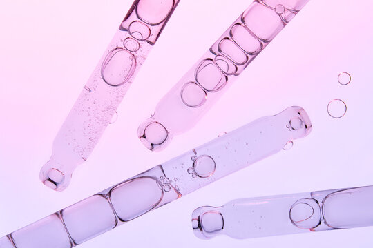 Several glass pipettes with liquid on gradient blue purple backdrop.