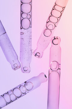 Several glass pipettes with liquid on gradient blue purple backdrop.