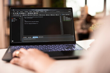 Closeup of programmer working from home, typing and debugging software code for app development. Young adult freelancer focused on project for tech company in apartment workspace.