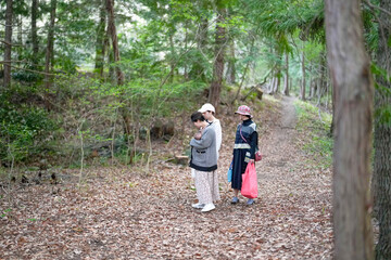 Obraz premium Three people are walking in a forest, one of them holding a baby. Scene is peaceful and serene, as the group is surrounded by nature and enjoying a quiet walk
