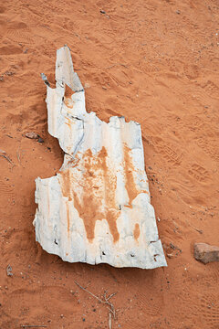 Weathered metal sheet showing rust and decay on a bed of red sand