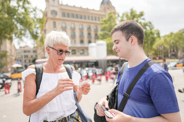 A man and a woman are standing on a street corner. The man is holding a cell phone and the woman is holding a drink. They are both smiling and seem to be enjoying their time together