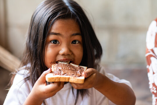 Girl eating chocolate bread inside rural Thai home