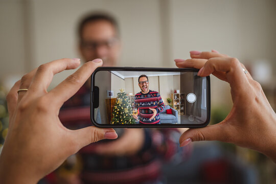 Woman taking photo of man making a toast during christmas video call - Powered by Adobe