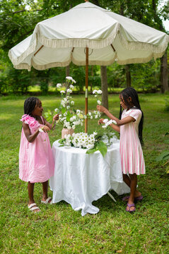 Two Girls Arranging Flowers Under a White Parasol in a Garden