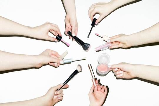 Hands holding various make up beauty products: blush, mascara, brushes