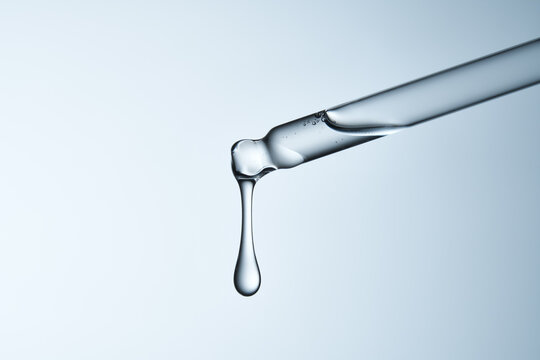 Clear glass pipette with a drop of liquid falling down. 