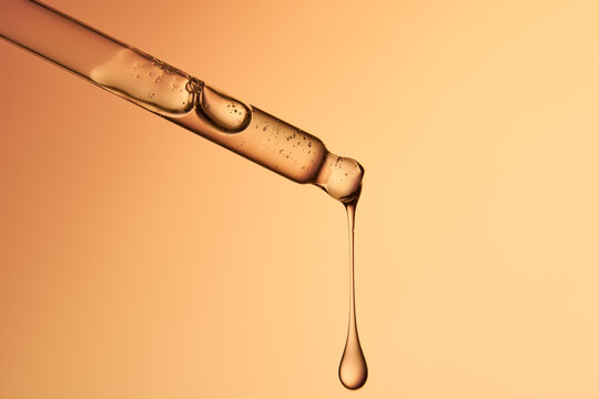 Clear glass pipette with a drop of liquid falling down. 
