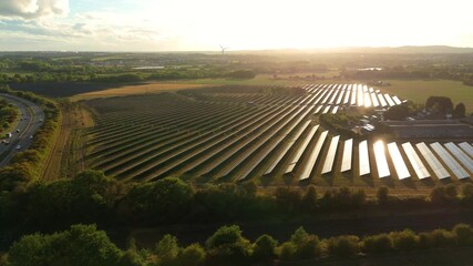 Aerial done view of solar power plant, photovoltaic panels generating renewable energy electricity in rural landscape at sunset with train passing along tracks, England UK - Powered by Adobe