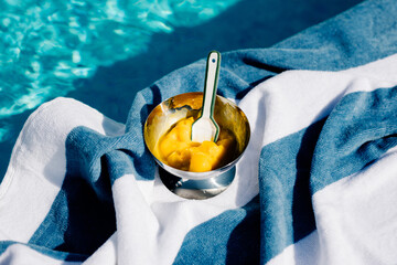 Metal cup with melting ice cream next to a swimming pool