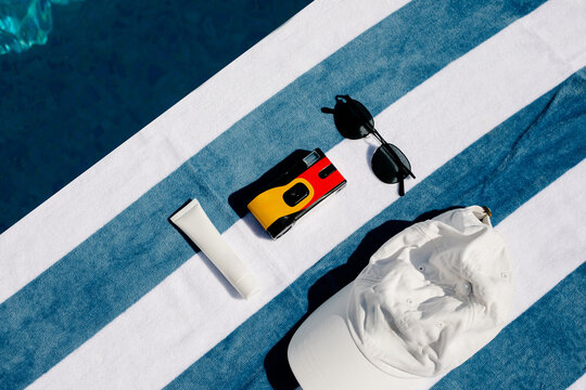 Top-down view of a hat, sunblock, a camera and sunglasses on a towel