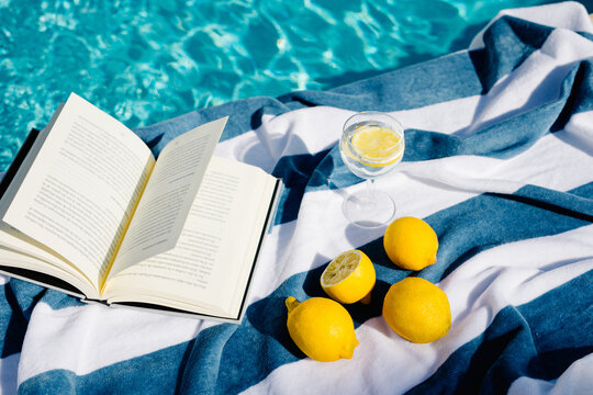 Still life composition of book, lemonade and lemons next to a pool
